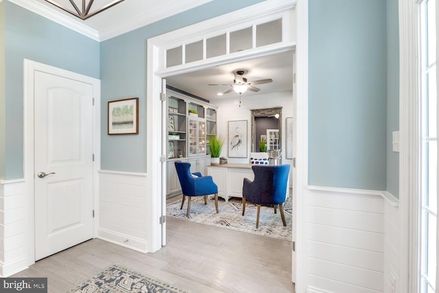 interior space featuring light wood-type flooring, a ceiling fan, crown molding, and wainscoting