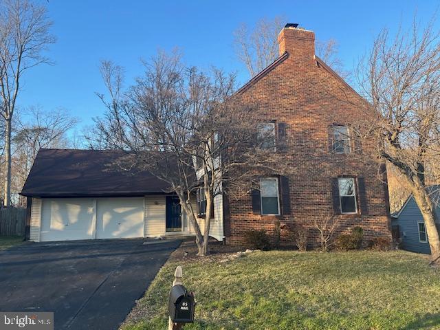 view of front of home with driveway, a front yard, a garage, brick siding, and a chimney