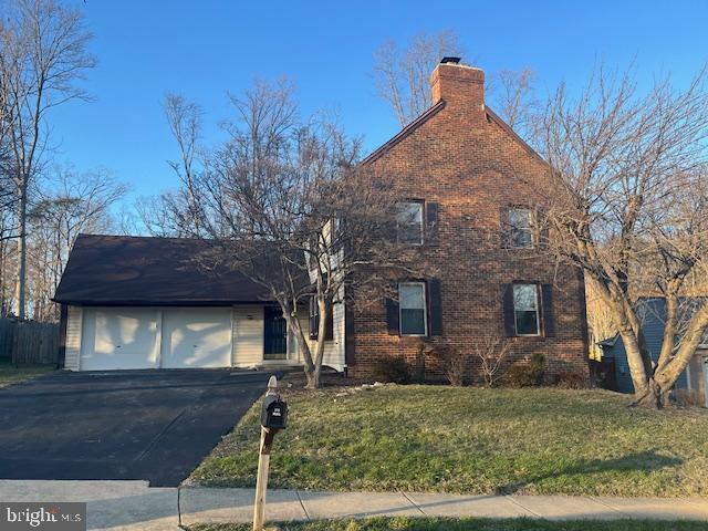 view of front of home featuring brick siding, a chimney, a garage, driveway, and a front lawn