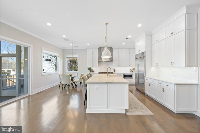 kitchen with white cabinets, dark wood-style floors, wall chimney exhaust hood, ornamental molding, and built in appliances