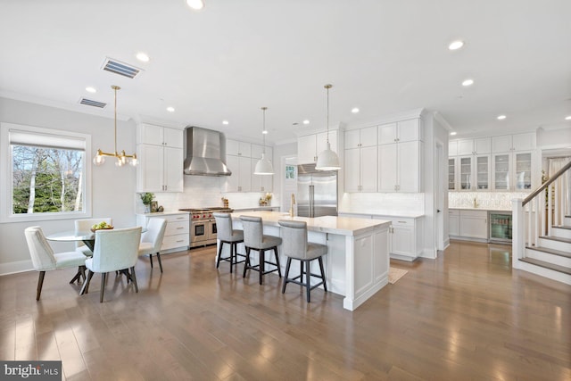 kitchen with wine cooler, high end appliances, visible vents, white cabinets, and wall chimney exhaust hood