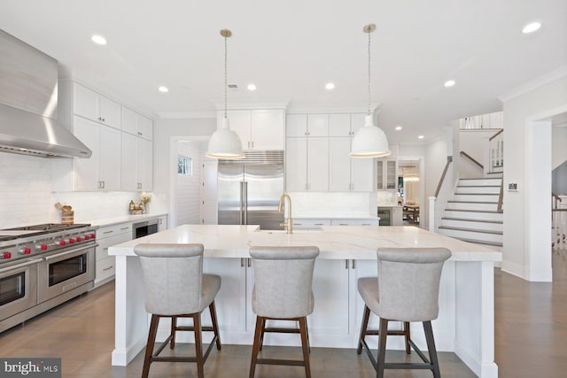 kitchen featuring wall chimney range hood, high quality appliances, white cabinetry, and a sink