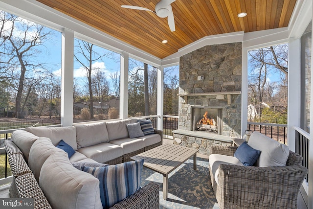 sunroom featuring vaulted ceiling, ceiling fan, an outdoor stone fireplace, and wooden ceiling