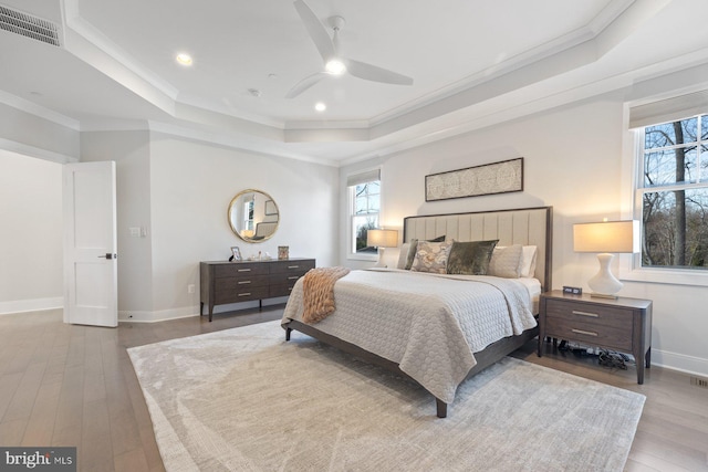 bedroom with a tray ceiling, wood finished floors, visible vents, and multiple windows