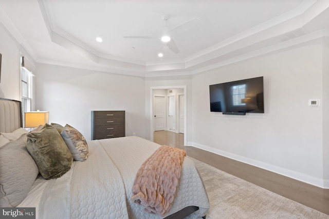 bedroom featuring crown molding, baseboards, a raised ceiling, and wood finished floors