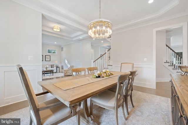 dining room with a notable chandelier, crown molding, a raised ceiling, wainscoting, and stairs