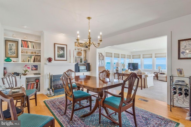 dining space with an inviting chandelier, a glass covered fireplace, visible vents, and light wood-style floors