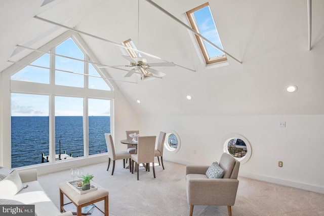 carpeted dining area with high vaulted ceiling, a water view, a skylight, a ceiling fan, and baseboards