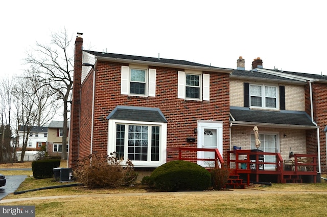 view of front of home with a front lawn, cooling unit, brick siding, and a chimney