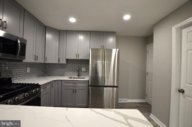 kitchen with tasteful backsplash, light stone counters, gray cabinets, stainless steel appliances, and a sink