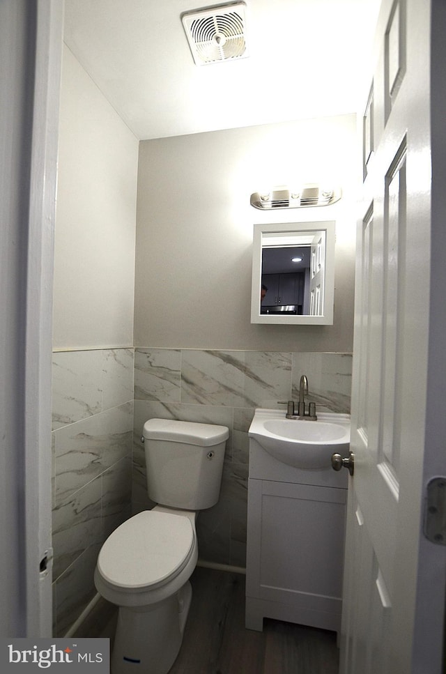 bathroom featuring vanity, wood finished floors, visible vents, tile walls, and toilet