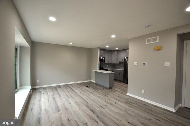 kitchen featuring stainless steel microwave, open floor plan, decorative backsplash, and freestanding refrigerator