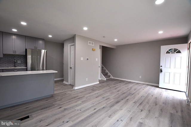 kitchen featuring light wood-type flooring, gray cabinetry, tasteful backsplash, freestanding refrigerator, and light countertops