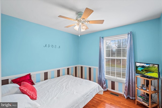 bedroom with ceiling fan, visible vents, baseboards, and wood finished floors