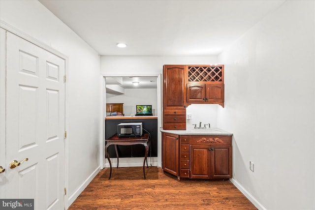 hall featuring dark wood finished floors, baseboards, and a sink