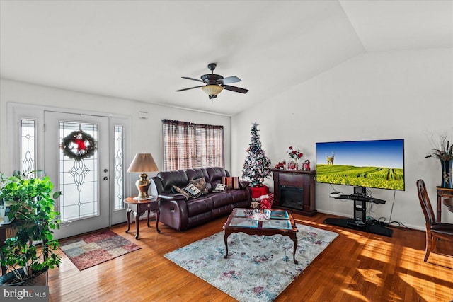 living area with a glass covered fireplace, wood finished floors, a ceiling fan, and vaulted ceiling