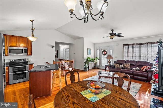 dining room with ceiling fan with notable chandelier, light wood-style flooring, and vaulted ceiling