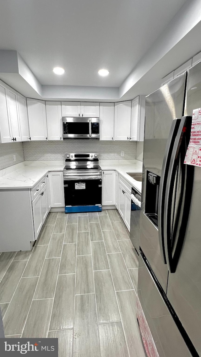 kitchen featuring backsplash, appliances with stainless steel finishes, white cabinets, a sink, and light stone countertops