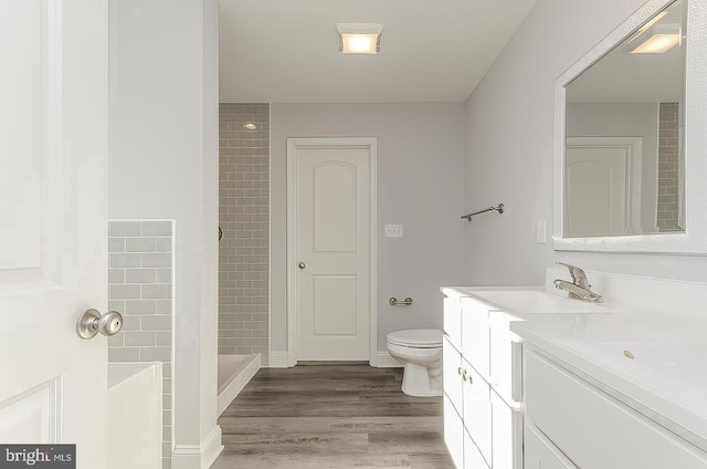 full bathroom featuring toilet, a tile shower, wood finished floors, and vanity