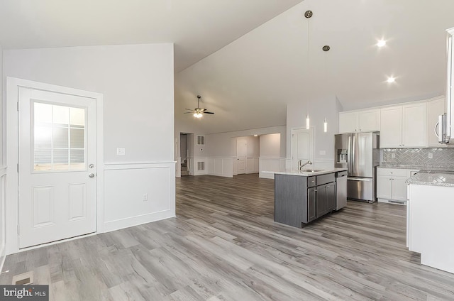 kitchen with white cabinets, a ceiling fan, open floor plan, vaulted ceiling, and stainless steel refrigerator with ice dispenser