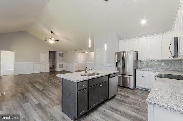 kitchen with a center island with sink, light stone countertops, stainless steel appliances, white cabinetry, and a sink