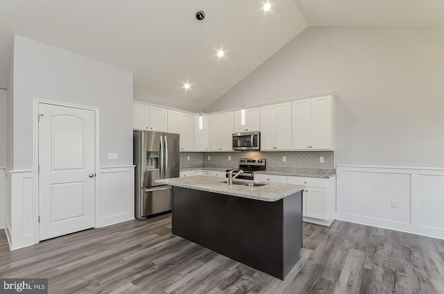 kitchen featuring a wainscoted wall, stainless steel appliances, white cabinets, a sink, and wood finished floors