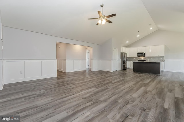 unfurnished living room featuring a ceiling fan, lofted ceiling, wainscoting, and dark wood-type flooring