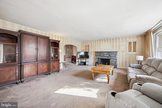 living area featuring arched walkways, a stone fireplace, and light carpet