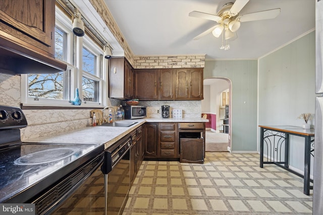 kitchen featuring arched walkways, ornamental molding, light countertops, black appliances, and a sink