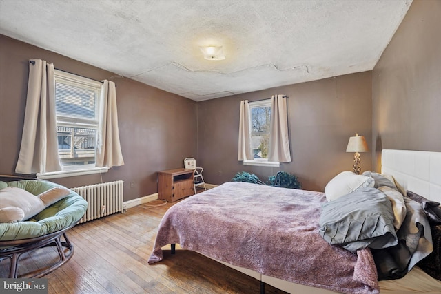 bedroom with radiator, multiple windows, baseboards, and hardwood / wood-style floors