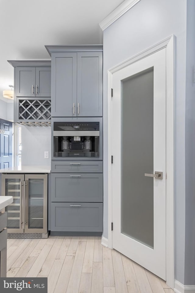 kitchen with beverage cooler, gray cabinets, oven, light countertops, and light wood-style floors