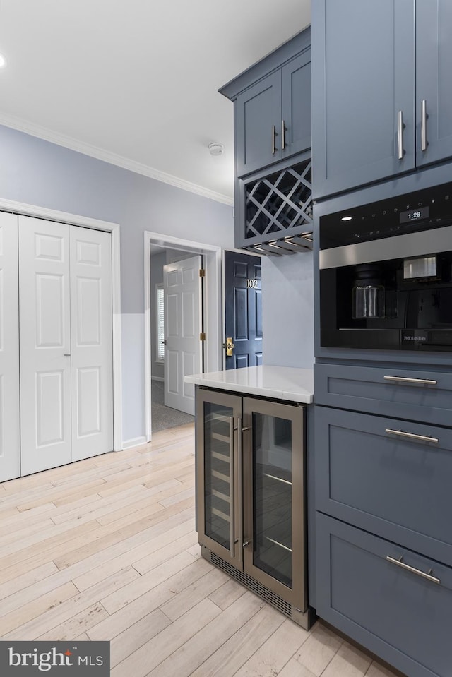 kitchen featuring light wood-style flooring, oven, ornamental molding, light countertops, and wine cooler