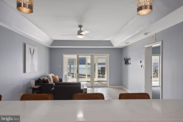 dining area with visible vents, a raised ceiling, wood finished floors, baseboards, and ceiling fan