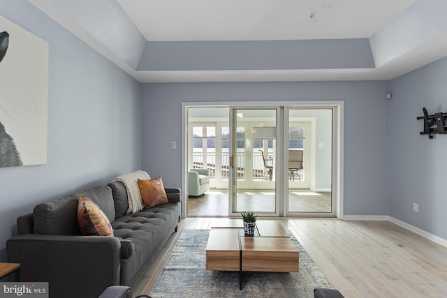 living area featuring a tray ceiling, baseboards, and light wood-style floors