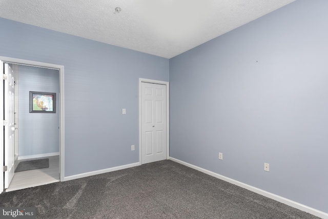 unfurnished bedroom with a closet, baseboards, dark carpet, and a textured ceiling