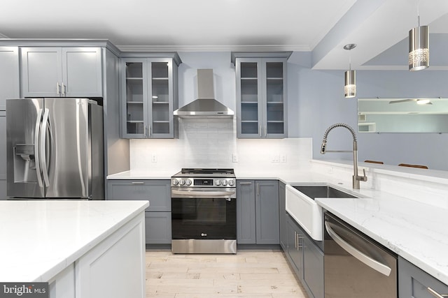 kitchen featuring wall chimney range hood, gray cabinets, appliances with stainless steel finishes, and a sink