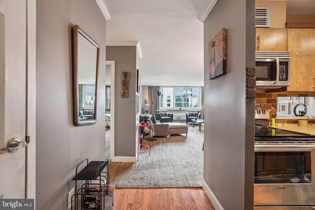 hall featuring visible vents, baseboards, crown molding, and wood finished floors