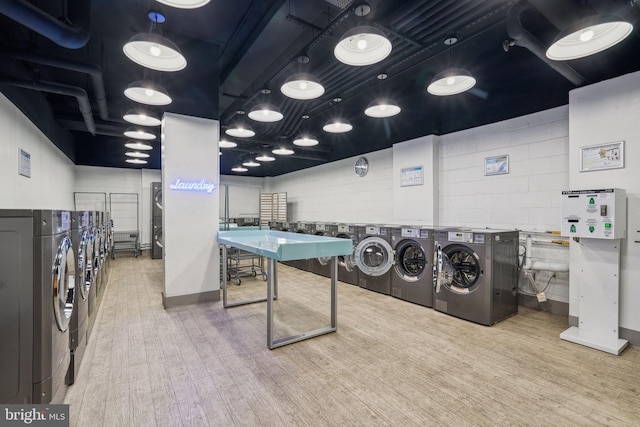 shared laundry area with concrete block wall, independent washer and dryer, and wood finished floors