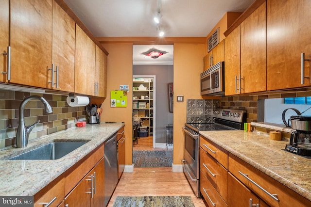 kitchen featuring stainless steel appliances, light stone counters, brown cabinetry, and a sink