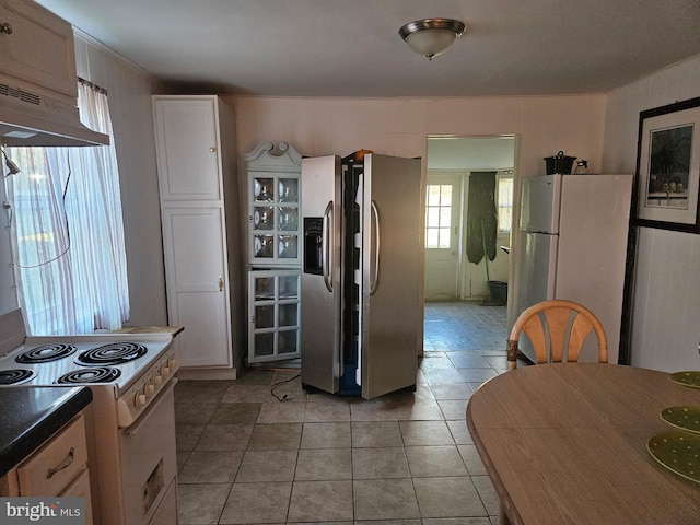 kitchen featuring dark countertops, light tile patterned flooring, white cabinetry, white appliances, and under cabinet range hood