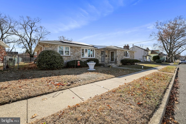 view of front of property with stone siding, roof mounted solar panels, fence, and a chimney