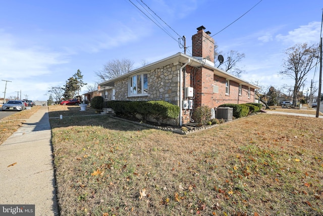 view of side of property with a lawn, stone siding, a chimney, cooling unit, and brick siding