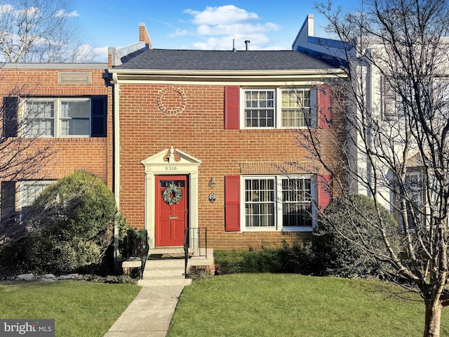 view of front facade featuring brick siding, roof with shingles, and a front yard