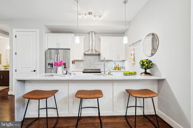kitchen featuring a kitchen breakfast bar, appliances with stainless steel finishes, wall chimney exhaust hood, white cabinets, and decorative backsplash