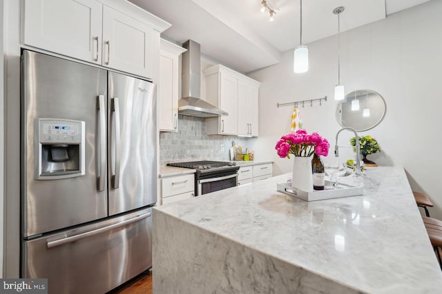 kitchen featuring wall chimney range hood, light stone counters, decorative backsplash, white cabinets, and stainless steel appliances