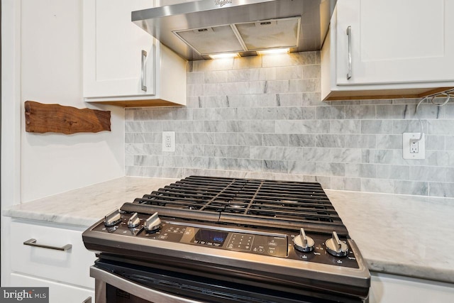 kitchen featuring tasteful backsplash, white cabinetry, wall chimney range hood, light stone countertops, and stainless steel range with gas stovetop