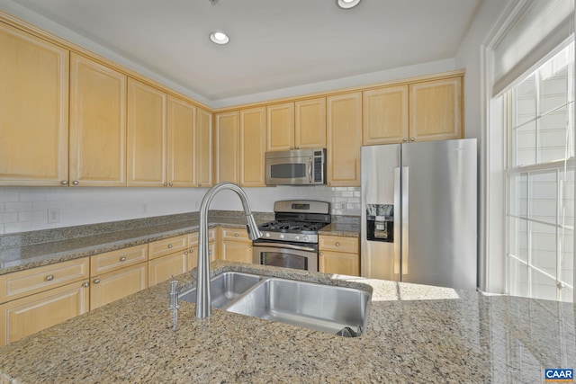 kitchen with appliances with stainless steel finishes, light brown cabinets, a sink, and light stone counters