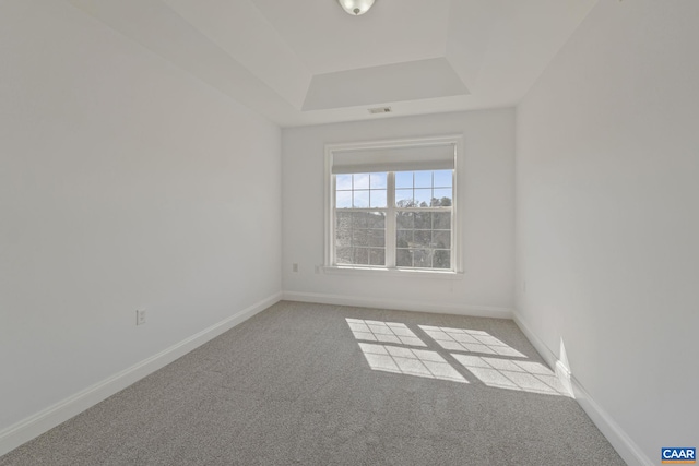 empty room featuring a raised ceiling, light colored carpet, visible vents, and baseboards