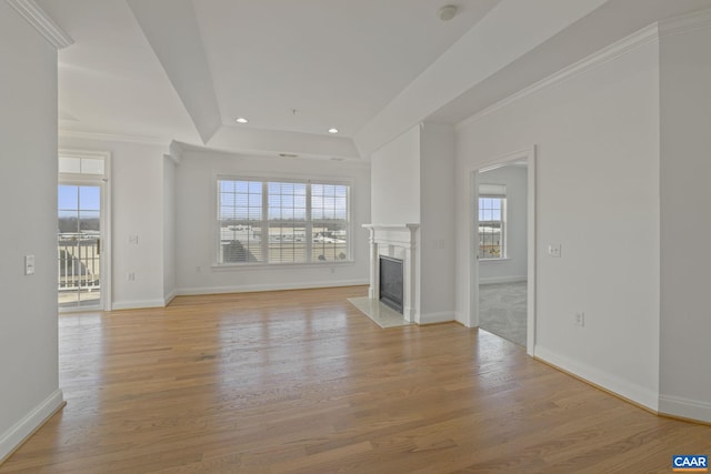 unfurnished living room featuring light wood finished floors, baseboards, a premium fireplace, a tray ceiling, and recessed lighting