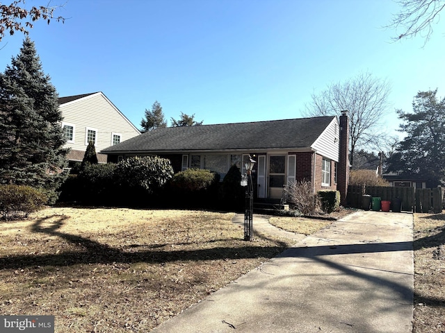 ranch-style house featuring brick siding, a chimney, and fence